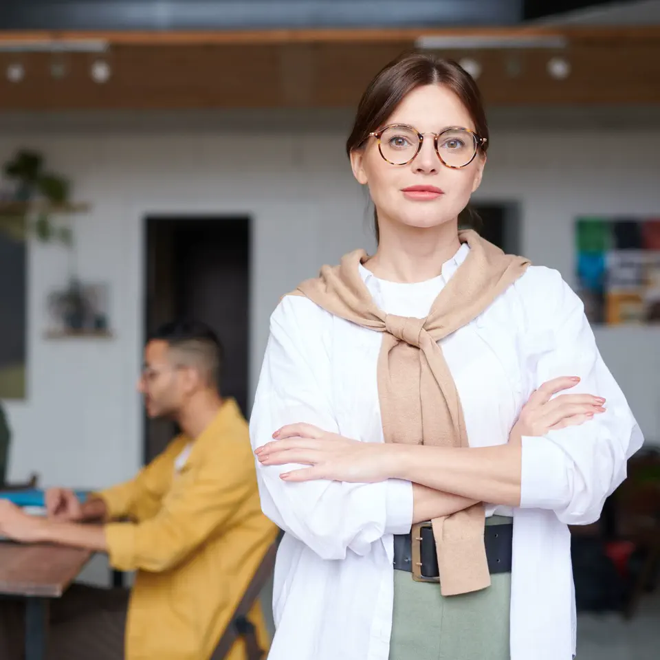 Nadia Brandt in tortoiseshell glasses, a sweater over her shoulders, standing in the studio
