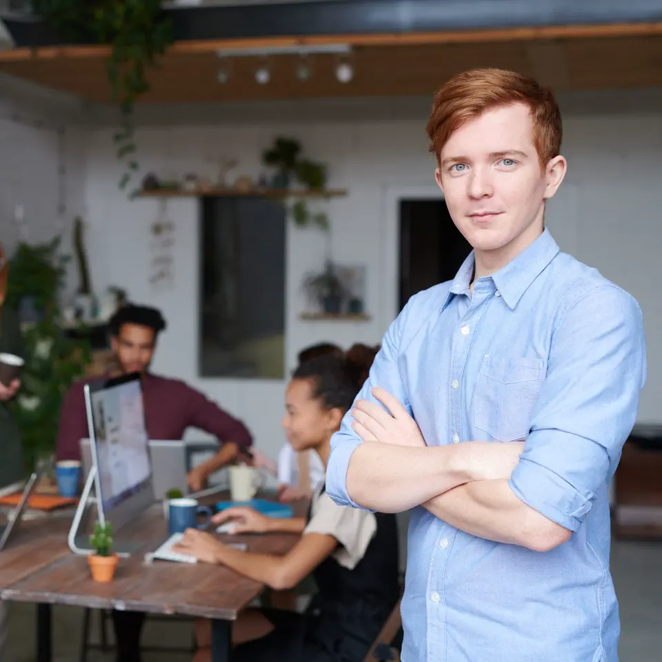 Owen Gallagher in a pale blue shirt, arms crossed, in front of the studio's work table
